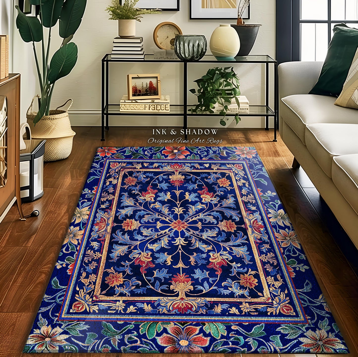 May include: A blue and gold patterned rug with a floral design. The rug has a dark blue background with gold accents and red and green flowers. The rug is on a wooden floor and there is a couch and a plant in the background. The text 'INK & SHADOW Original Fine Art Rugs' is visible in the image.