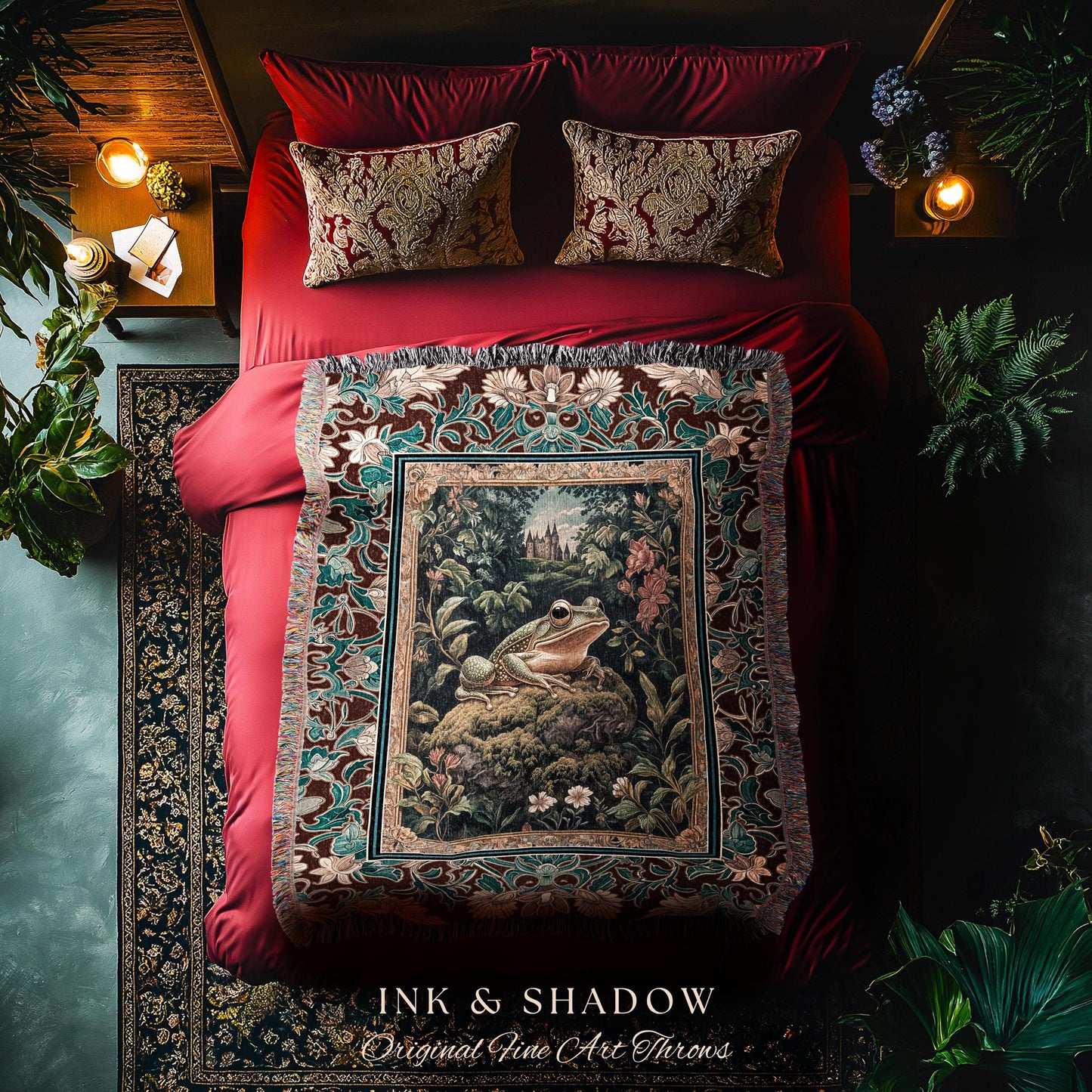 May include: A tapestry throw blanket with a dark red background and a green and brown floral pattern. The center of the tapestry features a green frog sitting on a rock in a forest setting. The tapestry has fringe around the edges. The text 'INK & SHADOW Original Fine Art Throws' is printed on the bottom of the tapestry.