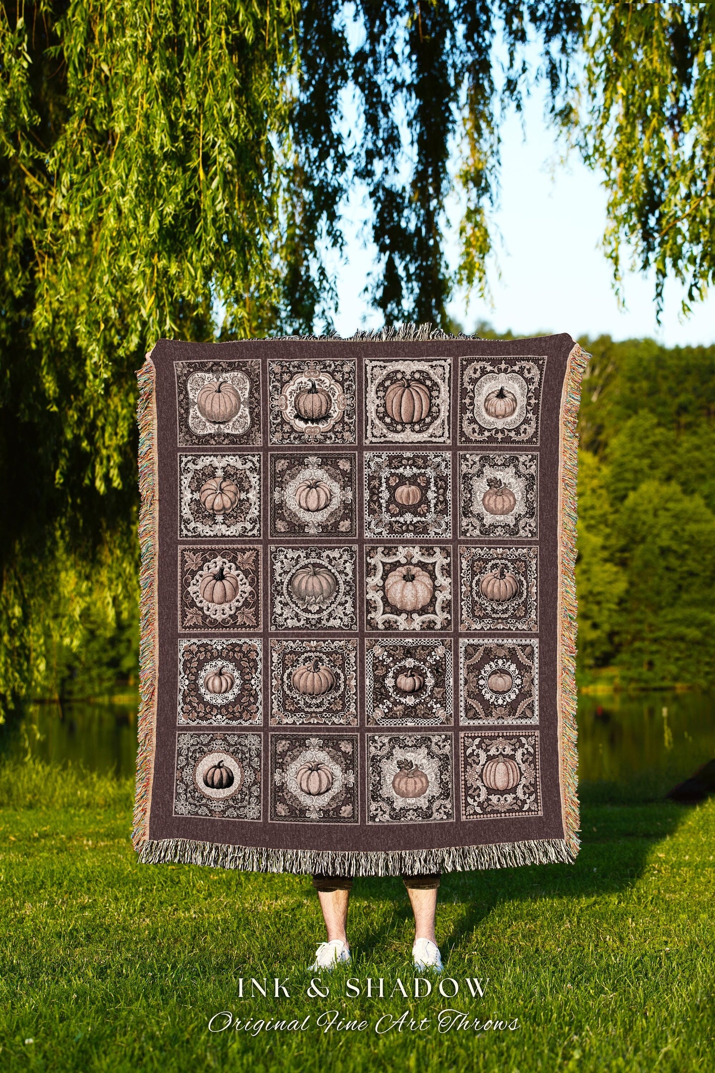 May include: A woven throw blanket with a brown background and a pattern of beige pumpkins in decorative frames. The text 'INK & SHADOW Original Fine Art Throws' is at the bottom of the blanket.