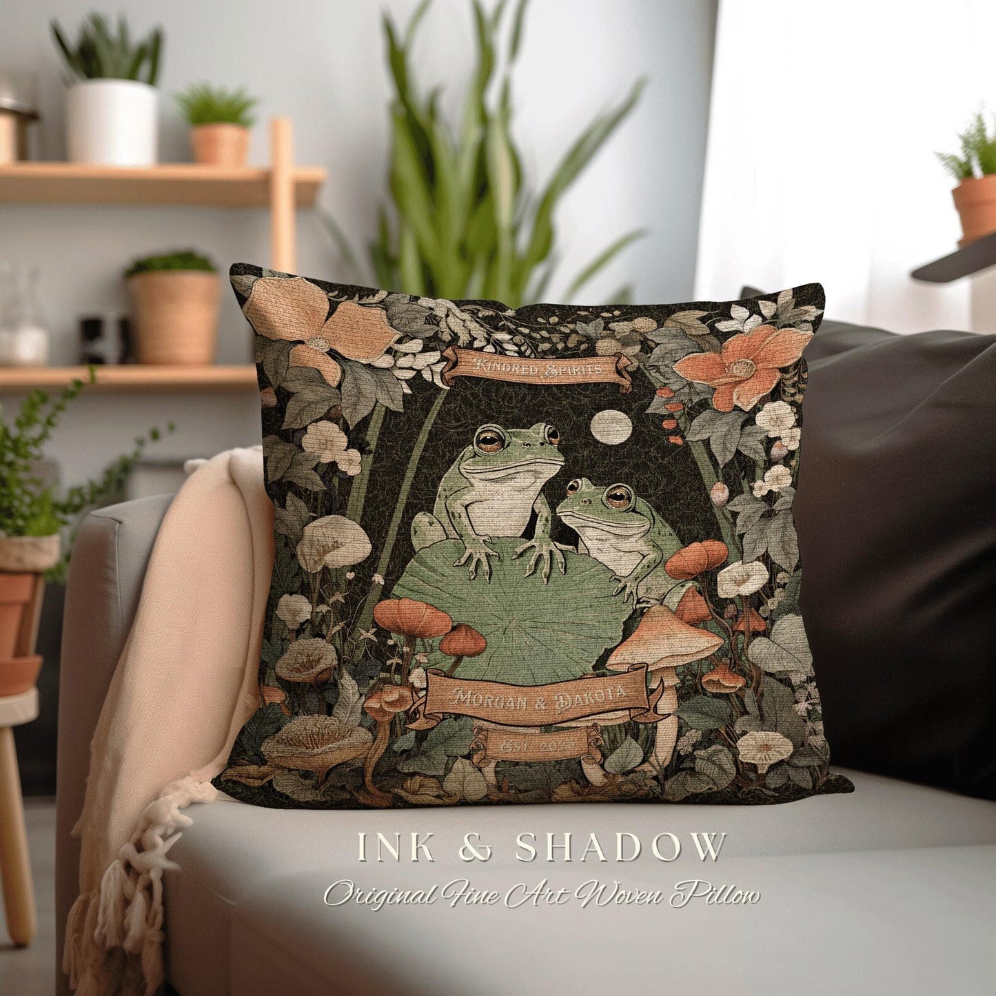 May include: A woven pillow with a dark green background featuring two green frogs sitting on a lily pad. The frogs are surrounded by flowers, mushrooms, and vines. The pillow has a banner that reads 'Kindred Spirits' and another banner that reads 'Morgan & Dakota Est. 2023'. The pillow is labeled 'Ink & Shadow Original Fine Art Woven Pillow'.