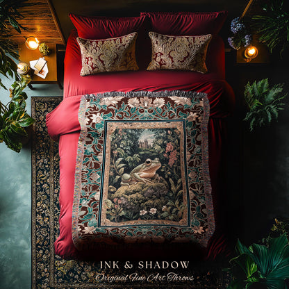 May include: A tapestry throw blanket with a dark red background and a green and brown floral pattern. The center of the tapestry features a green frog sitting on a rock in a forest setting. The tapestry has fringe around the edges. The text &#39;INK & SHADOW Original Fine Art Throws&#39; is printed on the bottom of the tapestry.