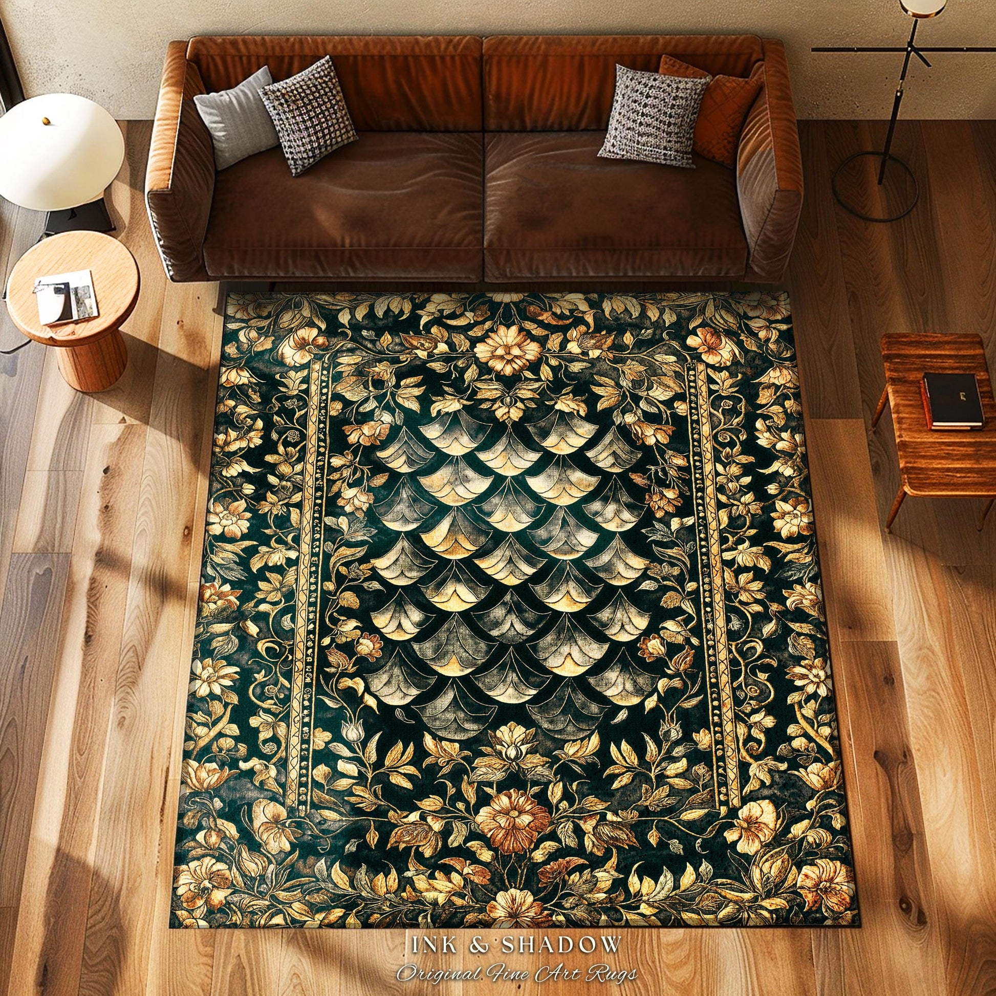 May include: A green rug with a gold floral border and a central design of overlapping gold and white scales. The rug is on a wooden floor and there is a brown leather couch in the background. The rug has the text &#39;INK & SHADOW Original Fine Art Rugs&#39; at the bottom.