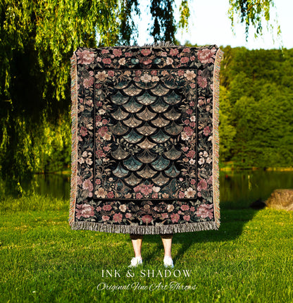May include: A woven tapestry throw blanket with a black background and a floral border. The center of the blanket features a pattern of overlapping teal and pink scales. The blanket has fringe along the bottom edge. The text &#39;INK & SHADOW Original Fine Art Throws&#39; is printed below the blanket.