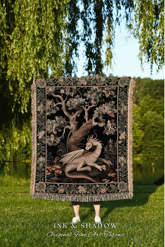 May include: A woven tapestry throw blanket with a black background featuring a white dragon curled around a tree trunk with green leaves. The throw blanket has a dark green, black, and pink border. The text &#39;INK & SHADOW Original Fine Art Throws&#39; is displayed below the blanket.