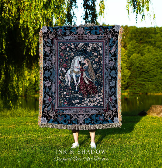 May include: A tapestry throw blanket with a dark blue background and a floral design. The center of the tapestry features a white unicorn and a woman in a red dress. The text &#39;INK & SHADOW Original Fine Art Throws&#39; is printed below the tapestry.