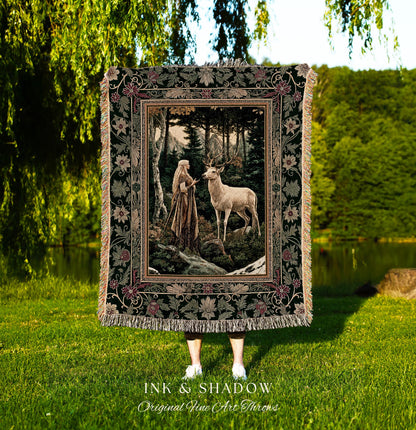 May include: A tapestry throw blanket with a dark green background and a floral border. The center of the tapestry features a woman in a long white dress standing in a forest with a white deer. The tapestry has the words &#39;Ink & Shadow Original Fine Art Throws&#39; at the bottom.
