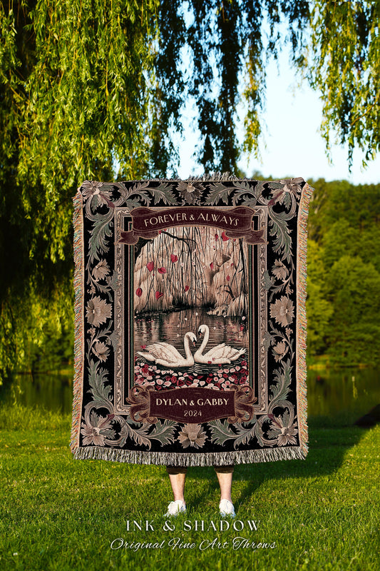 May include: A black tapestry throw blanket with a floral border. The center of the blanket features a pair of white swans on a lake with a willow tree in the background. The text &#39;Forever & Always&#39; is above the swans and the text &#39;Dylan & Gabby 2024&#39; is below the swans. The blanket is made by Ink & Shadow Original Fine Art Throws.