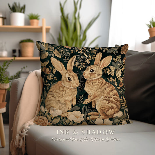 May include: A square throw pillow with a woven tapestry design featuring two brown rabbits in a green floral garden. The pillow is on a light gray couch with a beige throw blanket. The text &#39;INK & SHADOW Original Fine Art Woven Pillow&#39; is at the bottom of the image.