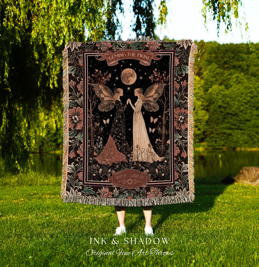 May include: A woven tapestry throw blanket with a dark background featuring two fairies with wings. The fairies are standing in a forest with a full moon and stars in the sky. The text on the blanket reads &#39;Gemini, The Twins&#39; and &#39;May 21st - June 20th&#39;. The blanket has a dark green, black, and brown color scheme with pink flowers on the border.