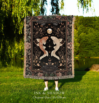 May include: A black woven throw blanket with a floral design and two gold fish. The blanket has a black border with the text &#39;PISCES THE FISH&#39; and &#39;FEB 19-MAR 20&#39; in white. The blanket is displayed in front of a green grassy background. The text &#39;INK & SHADOW Original Fine Art Throws&#39; is displayed below the blanket.