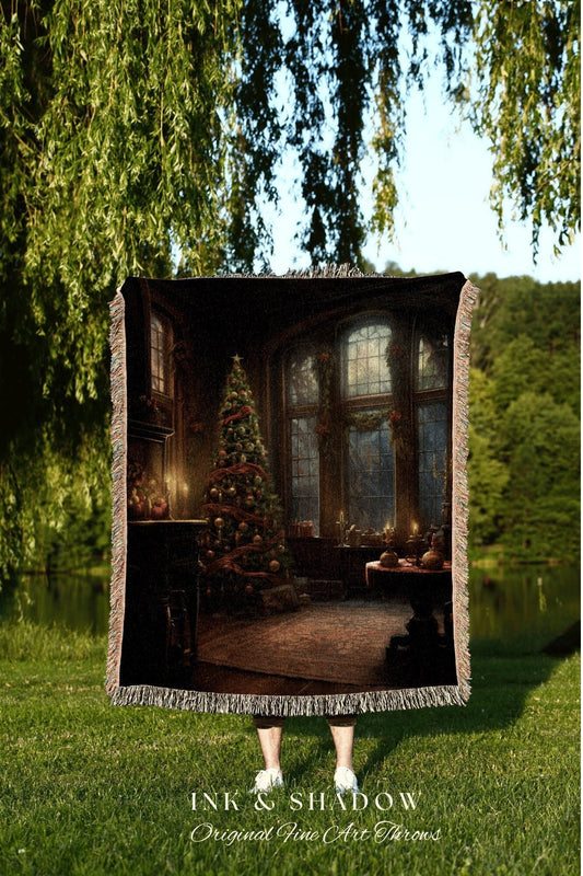May include: A woven tapestry throw blanket with a dark brown background featuring a Christmas tree and a large window with a view of a snowy forest. The text &#39;INK & SHADOW Original Fine Art Throws&#39; is printed at the bottom of the blanket.