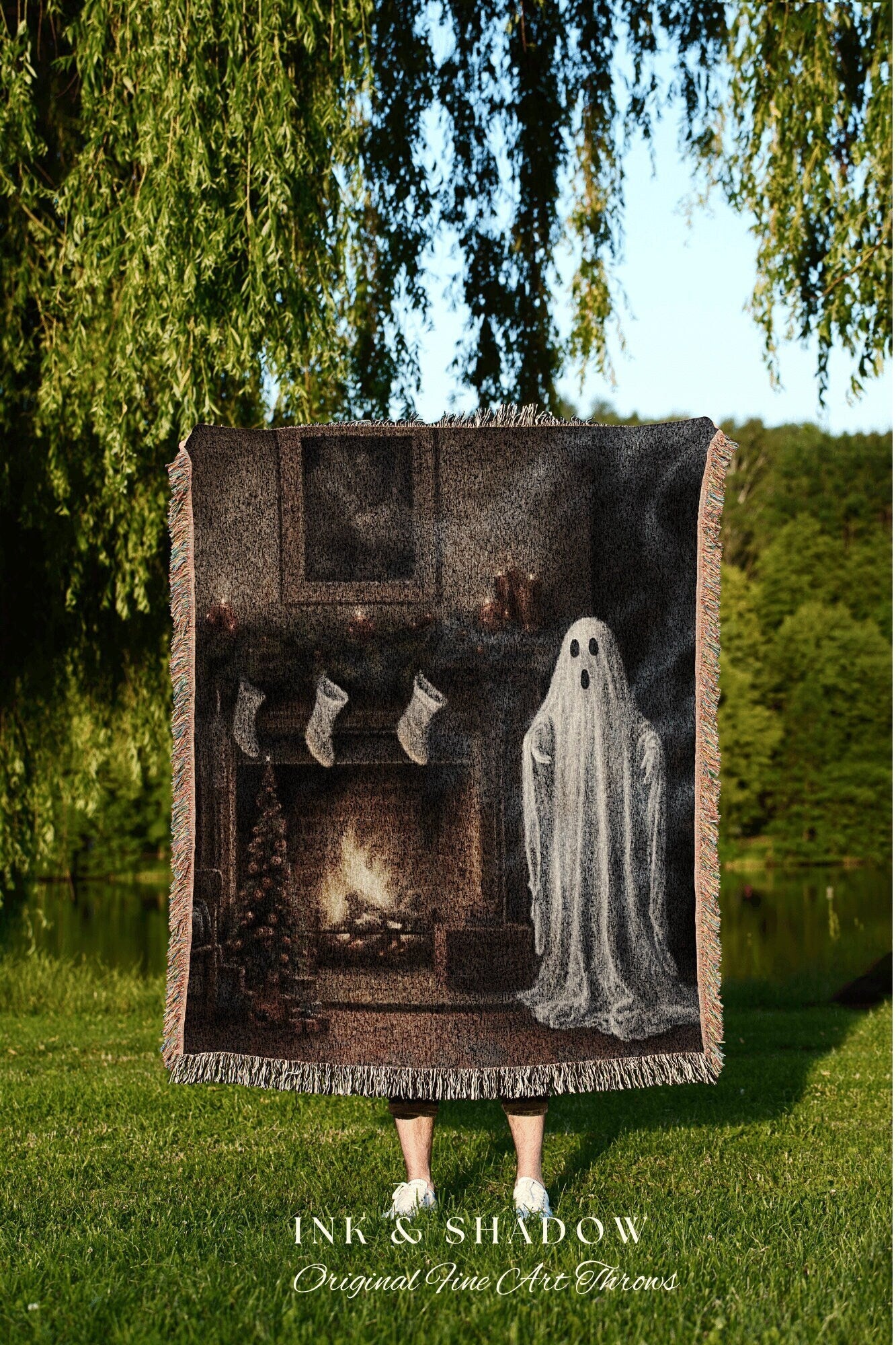 May include: A woven tapestry throw blanket with a dark brown background. The blanket features a fireplace with a fire burning, stockings hanging on the mantle, and a white ghost standing in front of the fireplace. The text &#39;INK & SHADOW Original Fine Art Throws&#39; is printed in white at the bottom of the blanket.