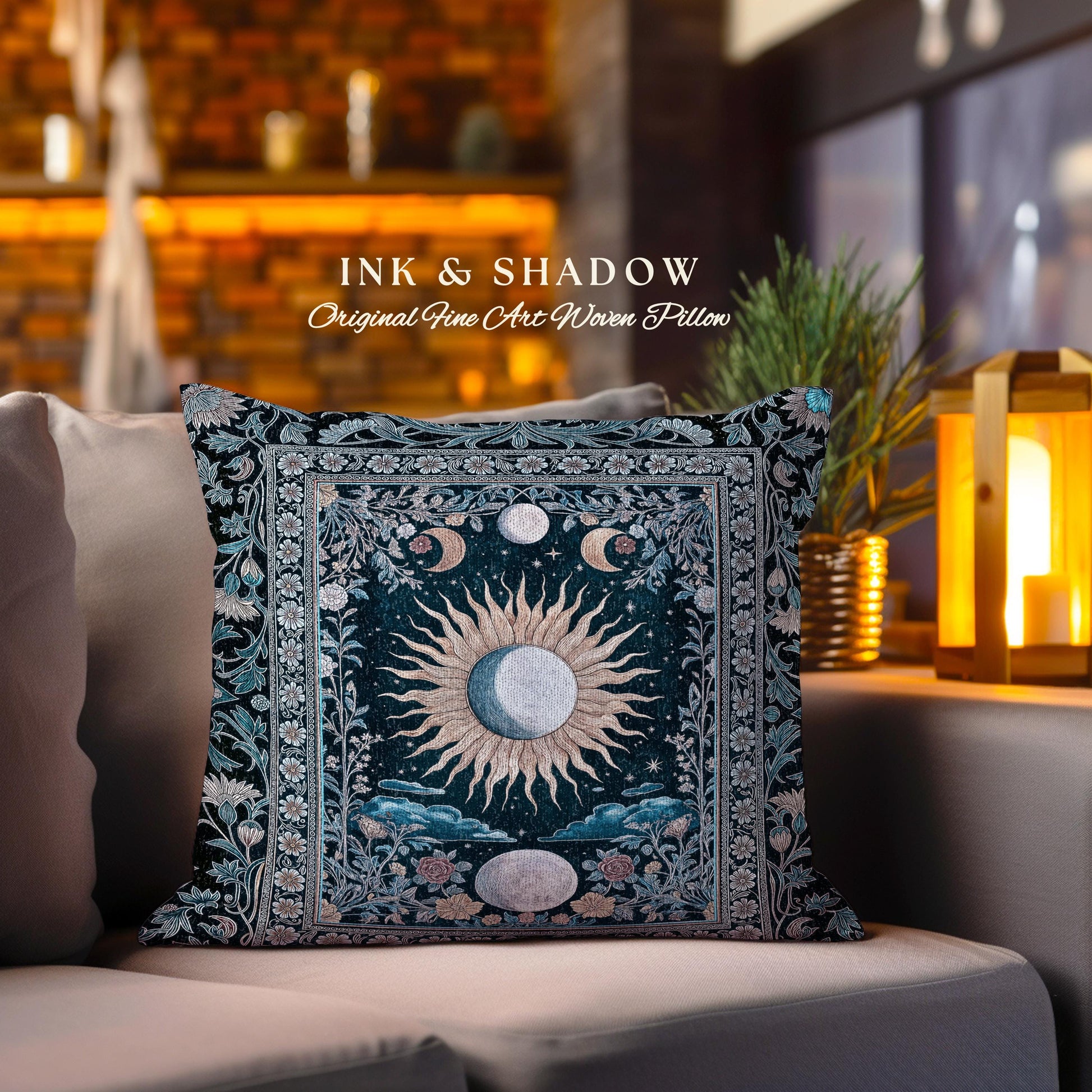 May include: A square pillow with a dark blue background and a woven design featuring a sun and moon with floral accents. The pillow has a border with a light blue and white floral pattern. The text &#39;INK & SHADOW Original Fine Art Woven Pillow&#39; is printed on the pillow.