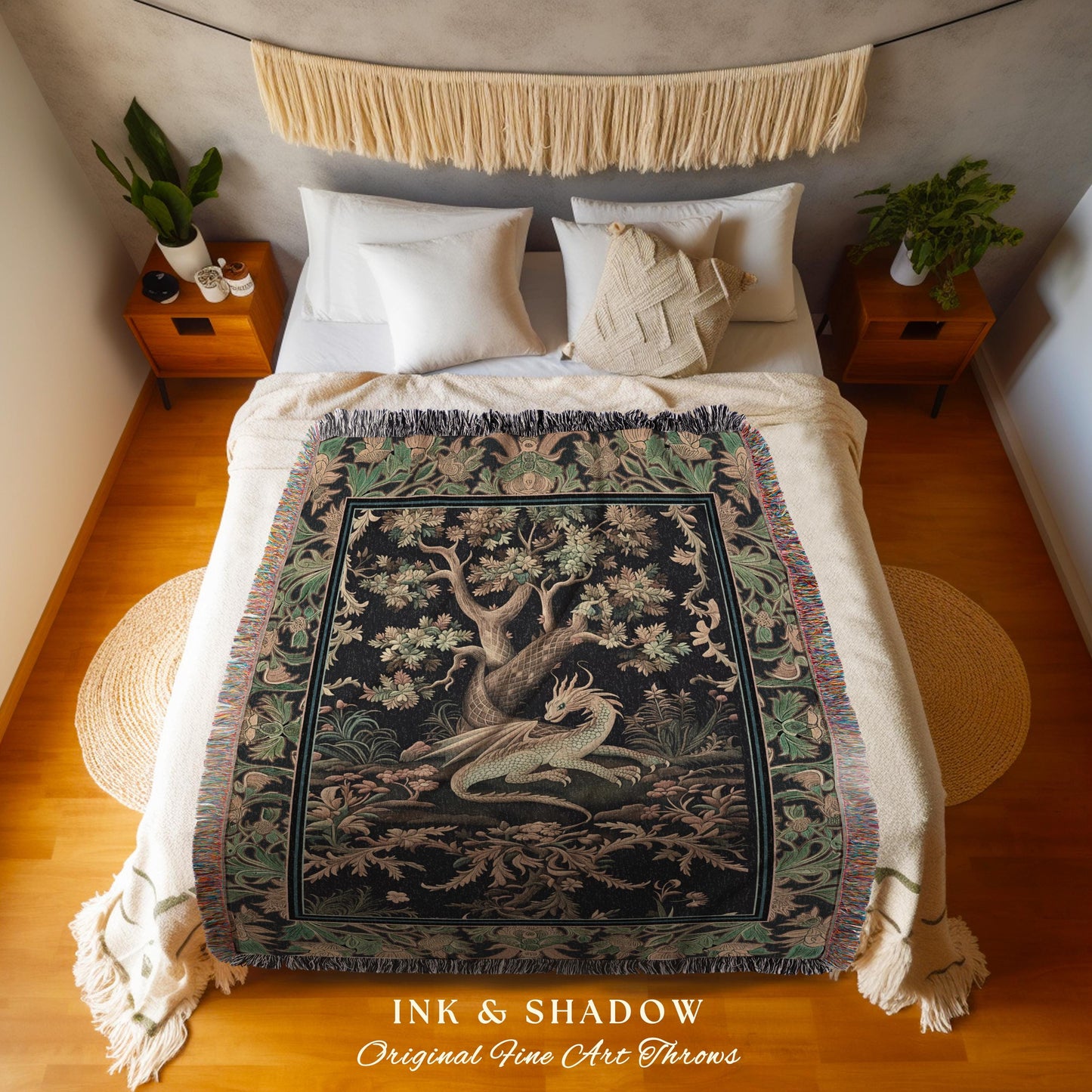 May include: A woven throw blanket with a black background and a green and gold tapestry design featuring a dragon and a tree. The throw blanket is on a bed with white bedding and a white and beige fringe trim. The text on the throw blanket reads &#39;INK & SHADOW Original Fine Art Throws&#39;.