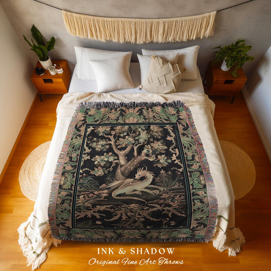May include: A woven throw blanket with a black background and a green and gold tapestry design featuring a dragon and a tree. The throw blanket is on a bed with white bedding and a white and beige fringe trim. The text on the throw blanket reads &#39;INK & SHADOW Original Fine Art Throws&#39;.