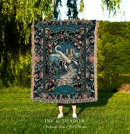 May include: A woven tapestry throw blanket with a dark blue background. The blanket features a white scorpion with a dark blue tail and a dark blue castle in the background. The blanket has a floral border with pink, white, and green flowers. The text on the blanket reads &#39;SCORPIO - THE SCORPION&#39; and &#39;OCT 23 - NOV 21&#39;. The text &#39;INK & SHADOW Original Fine Art Throws&#39; is printed below the blanket.