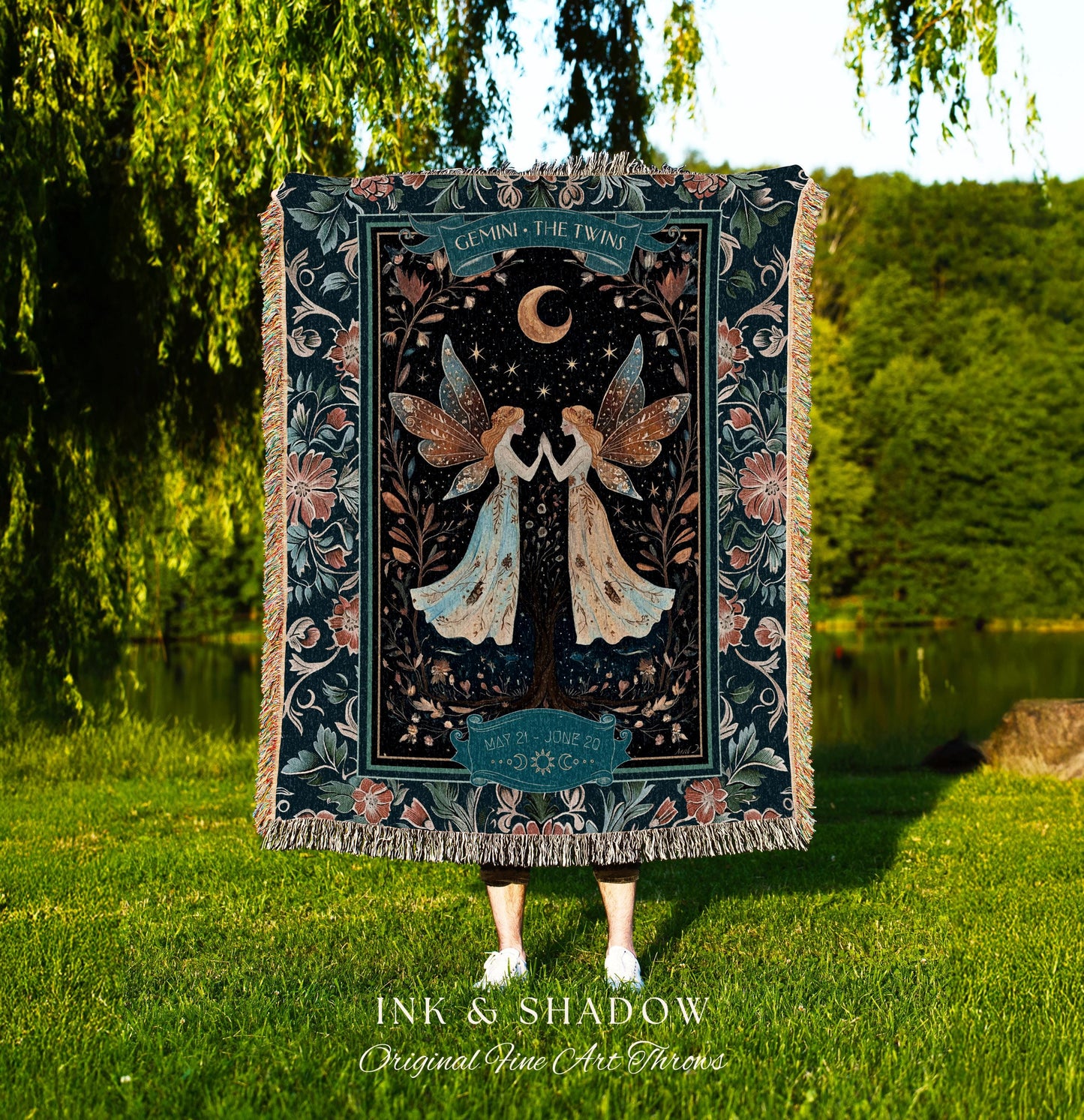 May include: A woven tapestry throw blanket with a dark blue background and a floral pattern. The center of the blanket features a design of two fairies with wings, a crescent moon, and stars. The text &#39;GEMINI - THE TWINS&#39; is at the top of the design. The text &#39;MAY 21 - JUNE 20&#39; is at the bottom of the design. The text &#39;INK & SHADOW Original Fine Art Throws&#39; is at the bottom of the blanket.