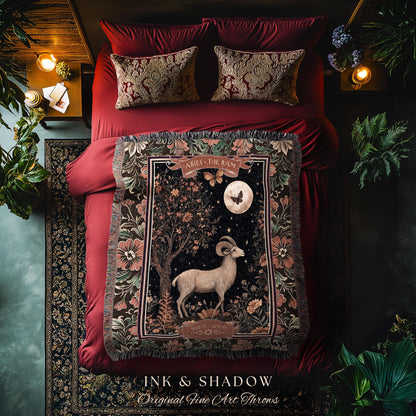 May include: A tapestry throw blanket with a dark background and a floral design. The center of the blanket features a white ram with a crescent moon and stars in the background. The text &#39;Aries - The Ram&#39; is at the top of the blanket. The blanket is displayed on a red bed with two pillows. The text &#39;INK & SHADOW Original Fine Art Throws&#39; is at the bottom of the blanket.