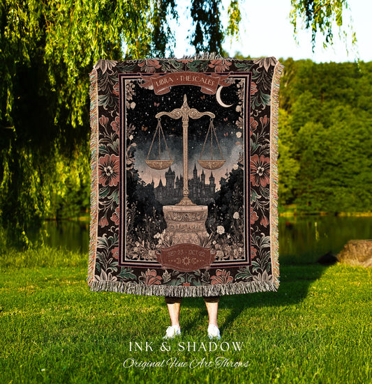 May include: A woven tapestry throw blanket with a dark background and a floral border. The center of the blanket features a black and white illustration of a scale with the text &#39;Libra - The Scales&#39; and &#39;Sept 23 - Oct 22&#39;.