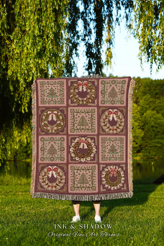 May include: A woven throw blanket features a repeating pattern of Christmas wreaths and evergreen trees in shades of burgundy, green, and beige. The throw is displayed against a backdrop of lush greenery and a body of water.  The text &#39;INK & SHADOW Original Fine Art Throws&#39; is visible at the bottom.