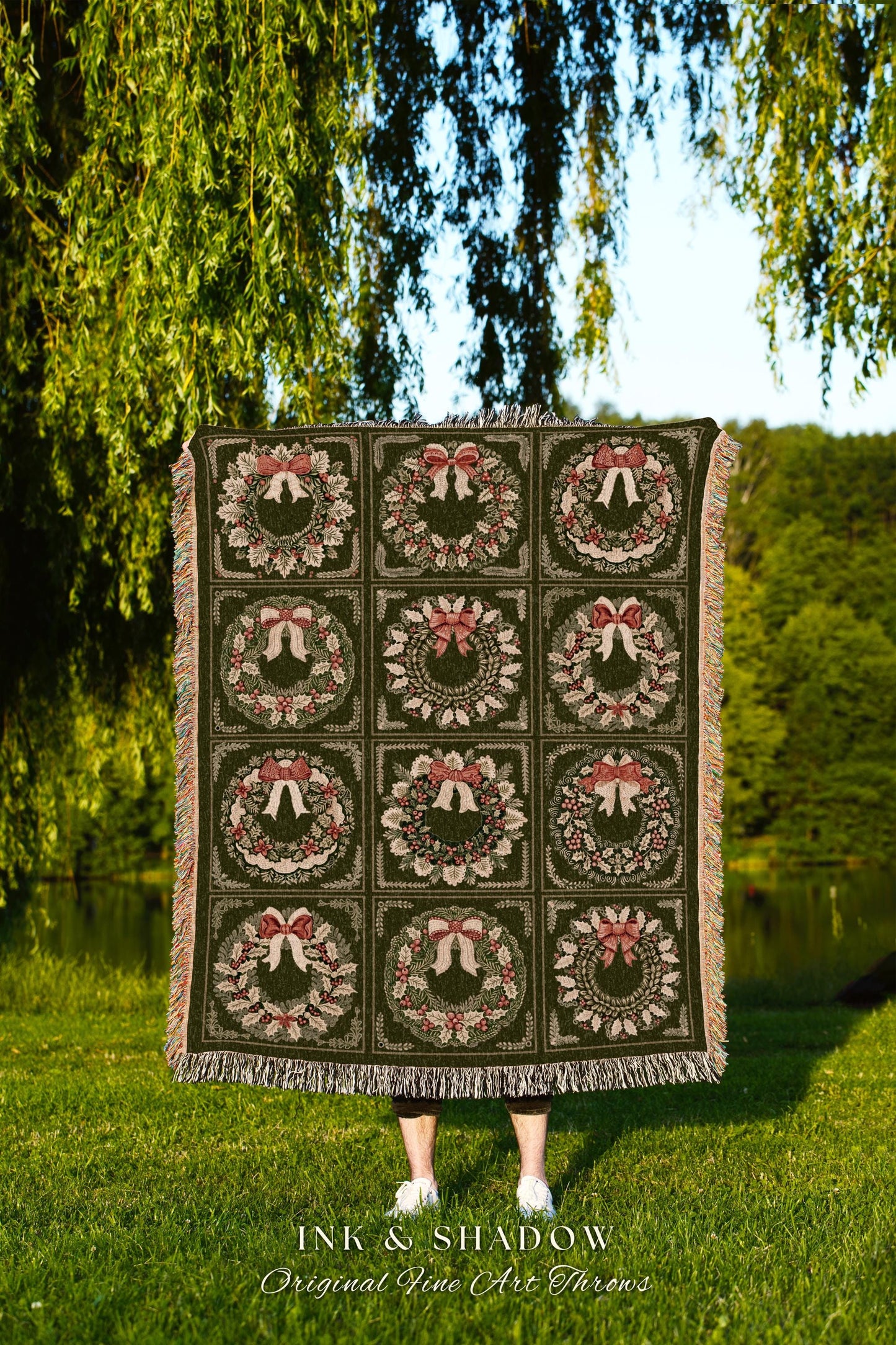 May include: A woven throw blanket with a green background and a repeating pattern of red and green wreaths with bows. The text &#39;INK & SHADOW Original Fine Art Throws&#39; is at the bottom of the blanket.