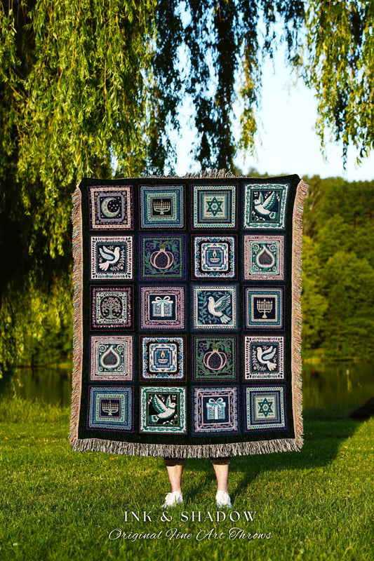 May include: A dark-colored woven throw blanket features a patchwork design with various symbols and images.  The squares contain images of doves, menorahs, pomegranates, stars of David, and other traditional Jewish symbols.  The blanket has a fringed edge.  The text &#39;INK & SHADOW Original Fine Art Throws&#39; is visible at the bottom.