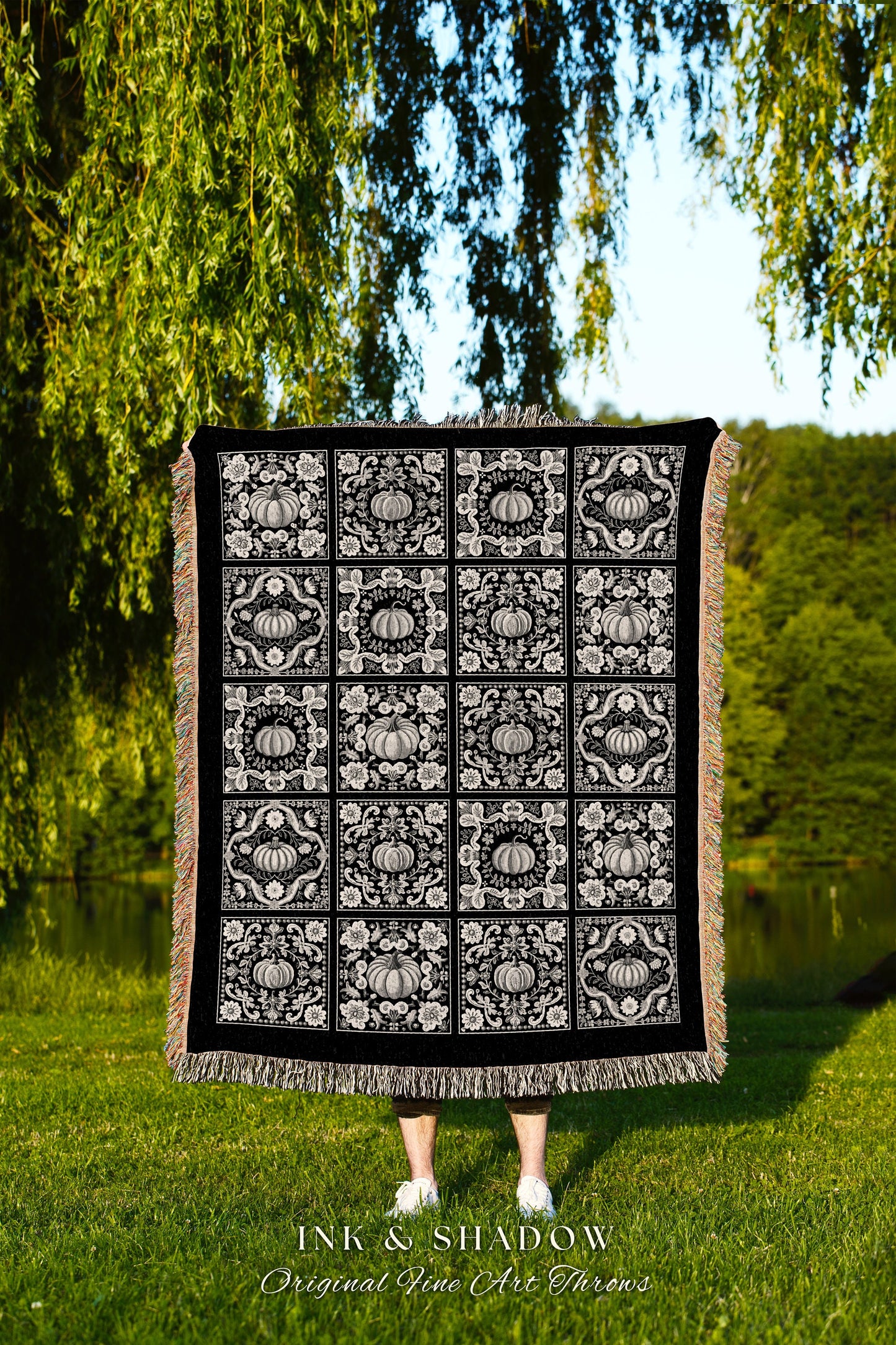 May include: A black woven throw blanket with a white pumpkin pattern. The blanket has a fringe border. The text &#39;INK & SHADOW Original Fine Art Throws&#39; is printed below the blanket.