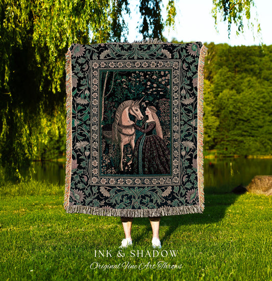 May include: A woven tapestry throw blanket with a black background and a green, pink, and white floral design. The center of the blanket features a scene of a woman in a long dress reaching out to a unicorn. The blanket has fringe on the edges and the words &#39;INK & SHADOW Original Fine Art Throws&#39; are printed at the bottom.