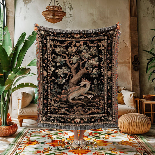 May include: A woven tapestry throw blanket with a black background and a detailed design of a tree and a dragon. The throw blanket has fringe around the edges and the text &#39;INK & SHADOW Original Fine Art Throws&#39; at the bottom.