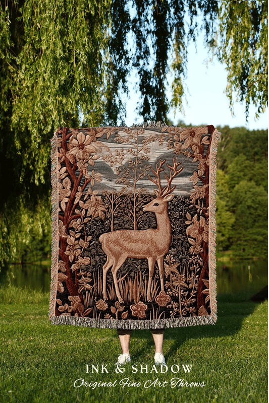 May include: A woven tapestry throw blanket with a brown deer standing in a forest scene. The throw blanket has a fringe border and features a brown deer with antlers standing in a forest with green trees and brown leaves. The text &#39;INK & SHADOW Original Fine Art Throws&#39; is at the bottom of the image.