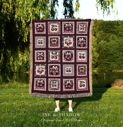 May include: A woven throw blanket with a burgundy background and a repeating pattern of framed cherries. The blanket is made of a soft, textured fabric and has a fringed edge. The text &#39;INK & SHADOW Original Fine Art Throws&#39; is printed at the bottom of the blanket.