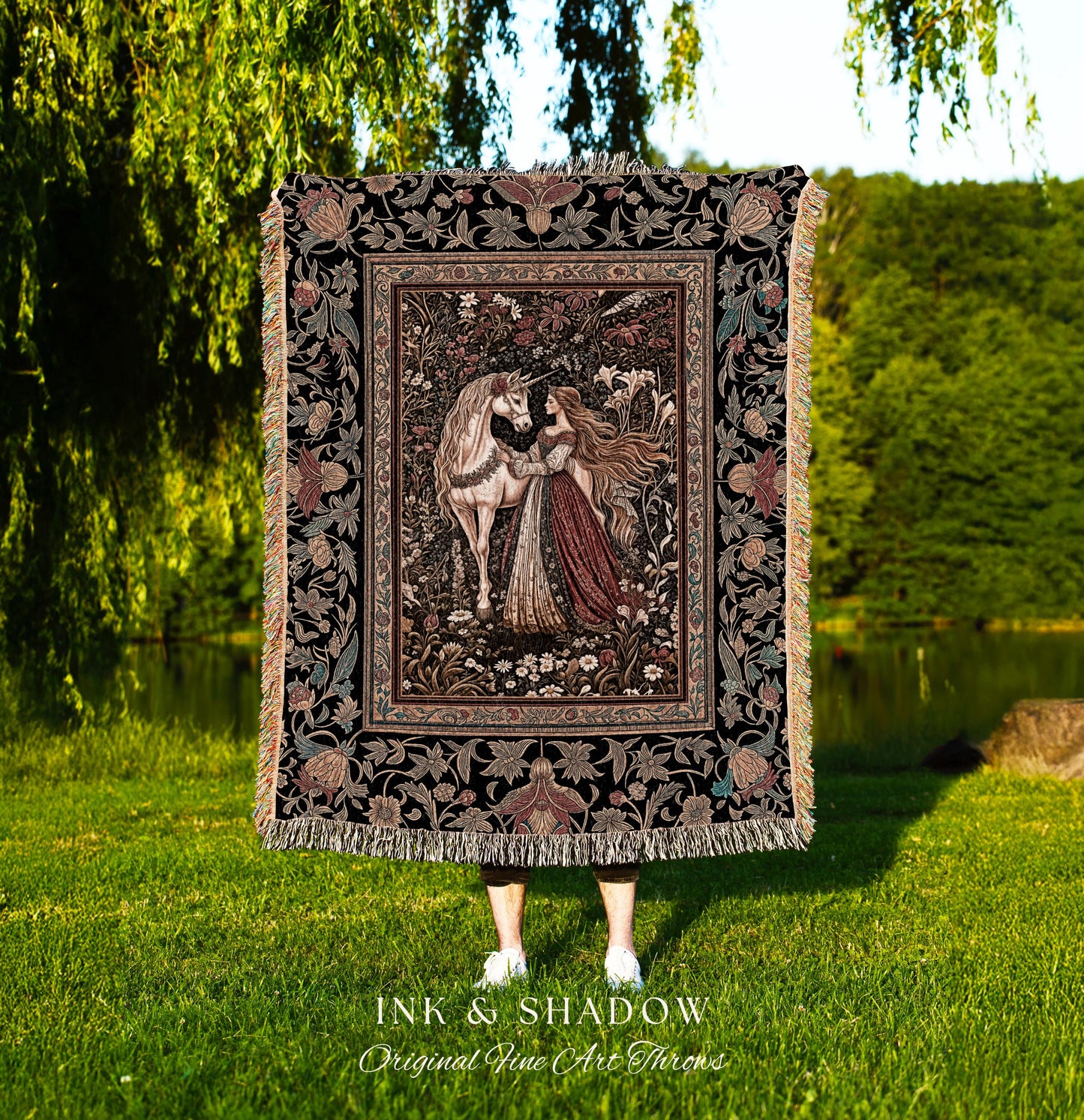 May include: A tapestry throw blanket with a black background and a colorful floral pattern. The center of the blanket features a woman in a red dress with long flowing hair, standing next to a white unicorn in a forest setting. The text &#39;INK & SHADOW Original Fine Art Throws&#39; is printed below the blanket.