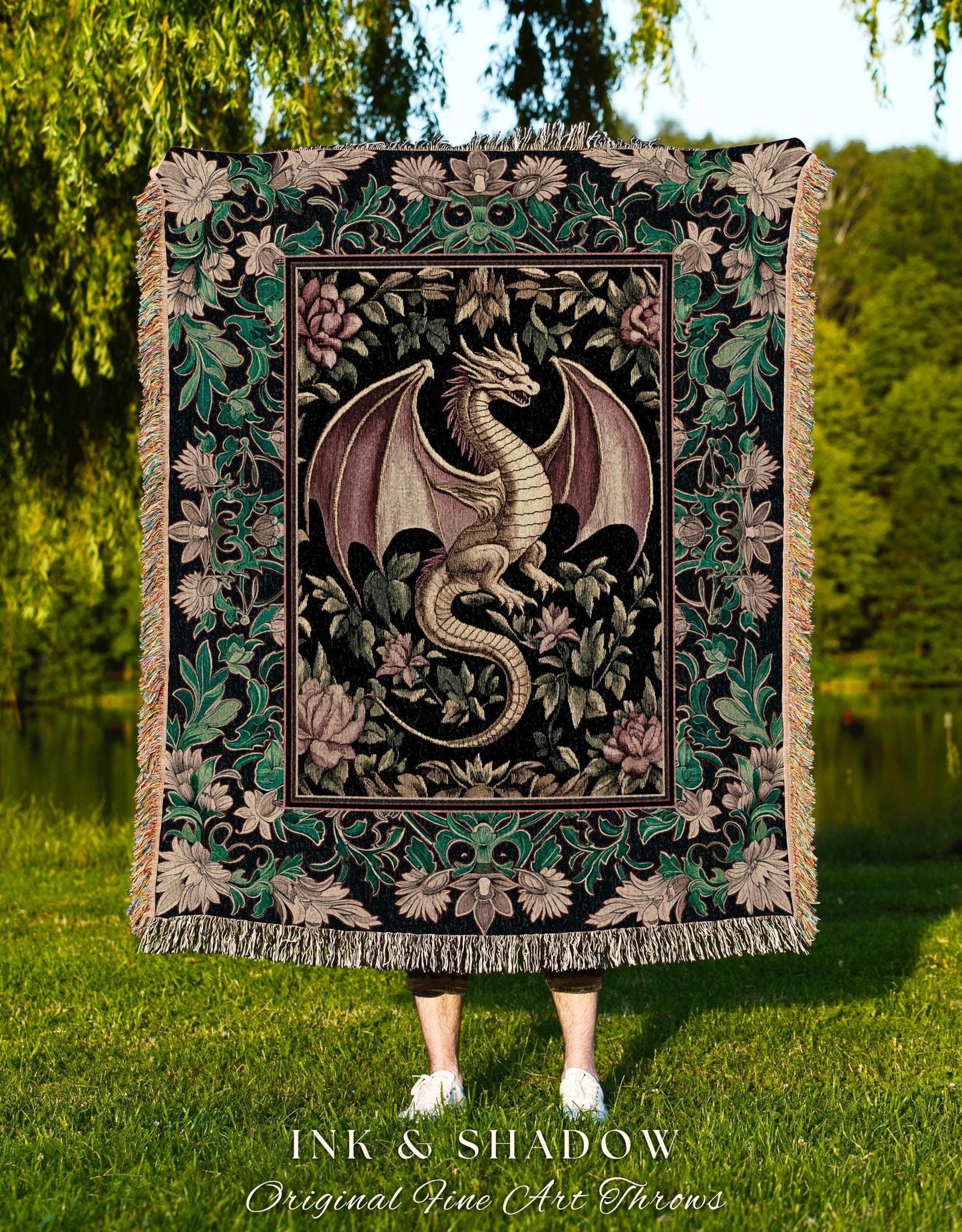 May include: A woven tapestry throw blanket with a black background and a green, pink, and gold floral pattern. A gold dragon with purple wings is in the center of the blanket. The blanket has fringe around the edges. The text &#39;INK & SHADOW Original Fine Art Throws&#39; is at the bottom of the blanket.