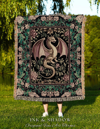 May include: A woven tapestry throw blanket with a black background and a green, pink, and gold floral pattern. A gold dragon with purple wings is in the center of the blanket. The blanket has fringe around the edges. The text &#39;INK & SHADOW Original Fine Art Throws&#39; is at the bottom of the blanket.