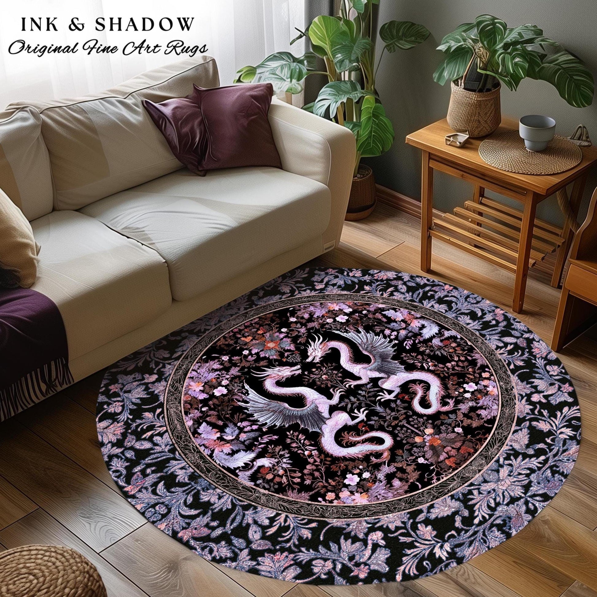 May include: A round rug with a black background and a pink and white floral design. Two pink and white dragons are facing each other in the center of the rug. The rug is surrounded by a black border with a floral design. The text &#39;INK & SHADOW Original Fine Art Rugs&#39; is in the top left corner of the image.