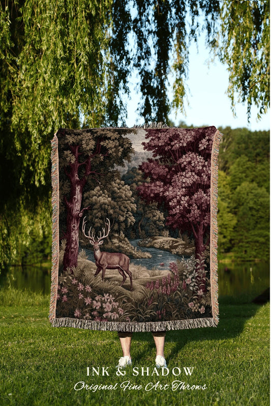 May include: A woven tapestry throw blanket with a forest scene featuring a deer, trees, and a river. The throw blanket has a fringed border and is in shades of brown, green, and purple. The text &#39;INK & SHADOW Original Fine Art Throws&#39; is at the bottom of the image.