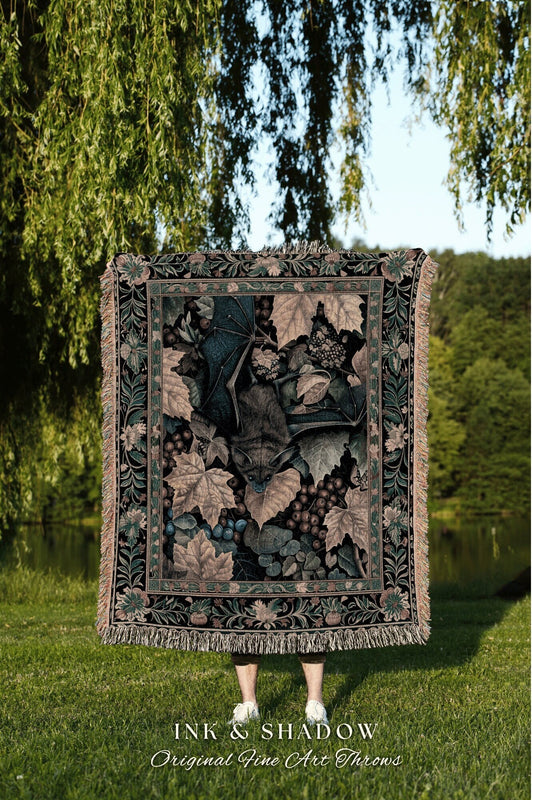 May include: A tapestry throw blanket with a black background and a detailed image of a bat flying through a vine with grapes. The tapestry has a dark green, brown, and beige color scheme. The text &#39;INK & SHADOW Original Fine Art Throws&#39; is printed below the blanket.
