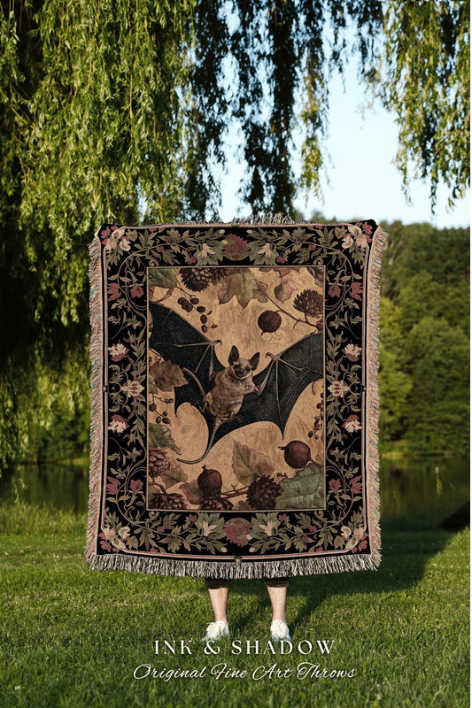 May include: A woven tapestry throw blanket with a black background and a tan center featuring a black bat with spread wings and a floral design. The text &#39;INK & SHADOW Original Fine Art Throws&#39; is at the bottom of the image.