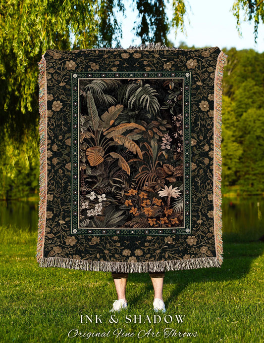 May include: A woven tapestry throw blanket with a dark green background and a floral pattern. The center of the blanket features a detailed illustration of a tropical jungle scene with palm trees, ferns, and flowers in shades of green, brown, and orange. The blanket has a fringed border and the words &#39;INK & SHADOW Original Fine Art Throws&#39; are printed below the blanket.