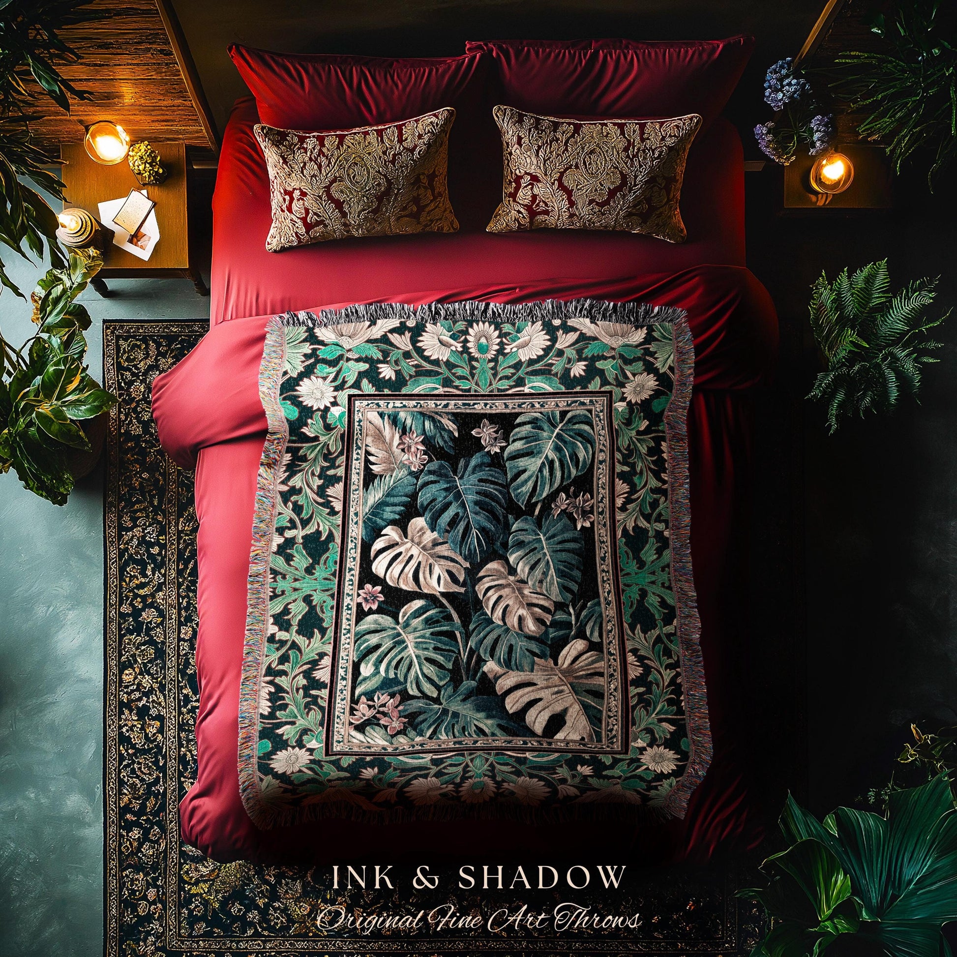May include: A green and black throw blanket with a floral pattern. The blanket has a fringe border and is displayed on a red velvet bed. The blanket has the text &#39;INK & SHADOW Original Fine Art Throws&#39; at the bottom.