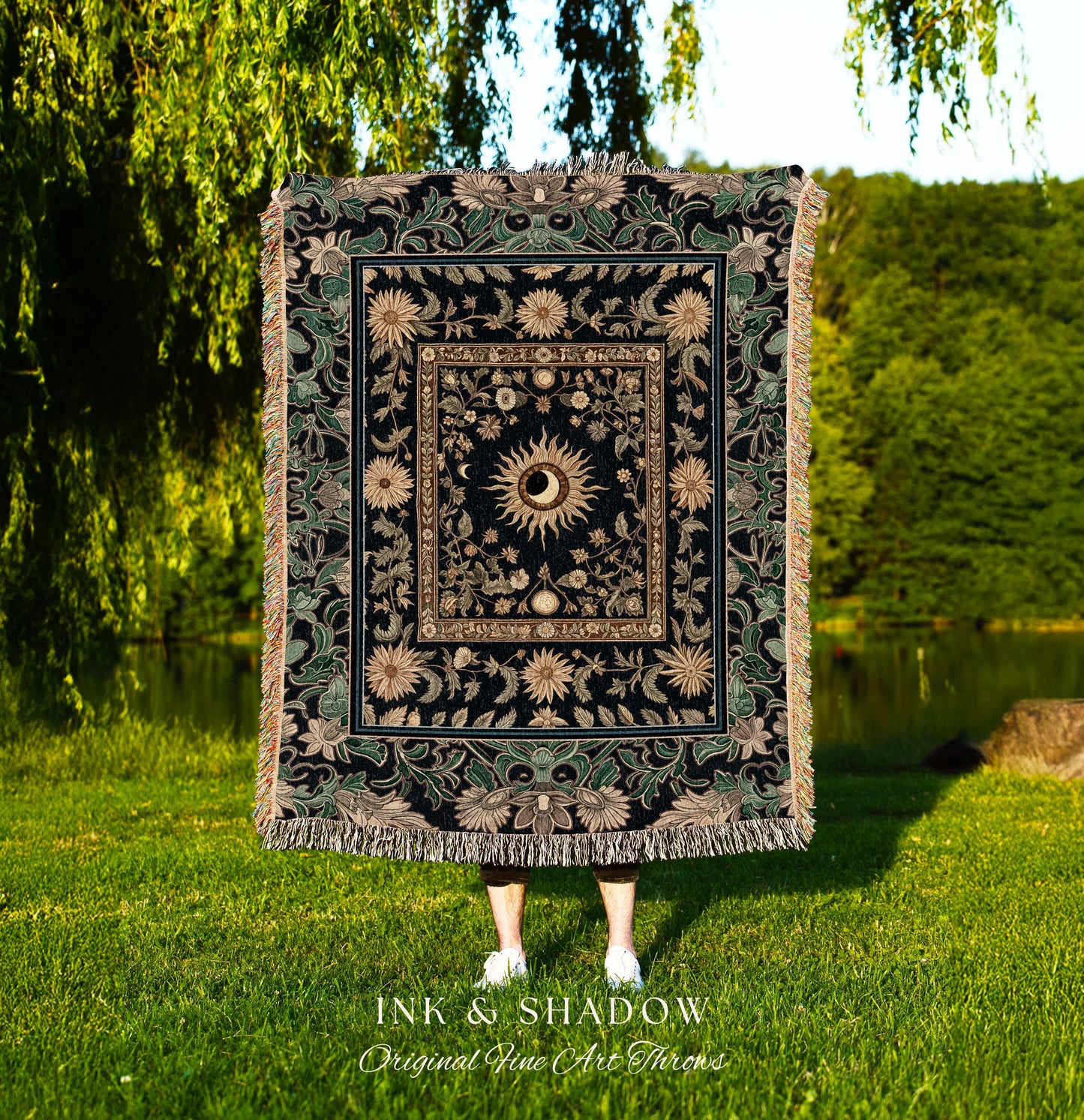 May include: A black woven tapestry throw blanket with a gold and green floral design. The center of the blanket features a large sun with a human eye in the center. The text &#39;INK & SHADOW Original Fine Art Throws&#39; is printed below the blanket.