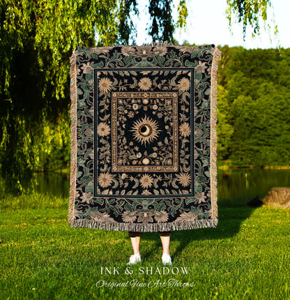 May include: A black woven tapestry throw blanket with a gold and green floral design. The center of the blanket features a large sun with a human eye in the center. The text &#39;INK & SHADOW Original Fine Art Throws&#39; is printed below the blanket.