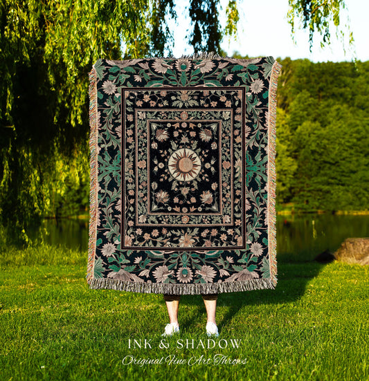 May include: A woven tapestry throw blanket with a black background and a gold sun in the center. The sun is surrounded by pink and green floral designs. The blanket has a fringe border and is made of a soft, luxurious fabric. The text &#39;INK & SHADOW Original Fine Art Throws&#39; is printed below the blanket.