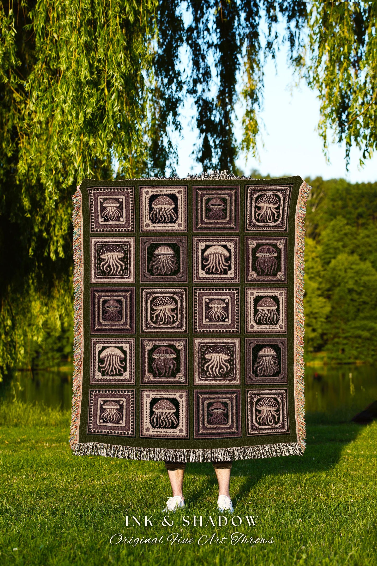 May include: A woven tapestry throw blanket with a dark green background and a repeating pattern of brown jellyfish in square frames. The text &#39;INK & SHADOW Original Fine Art Throws&#39; is printed at the bottom of the blanket.