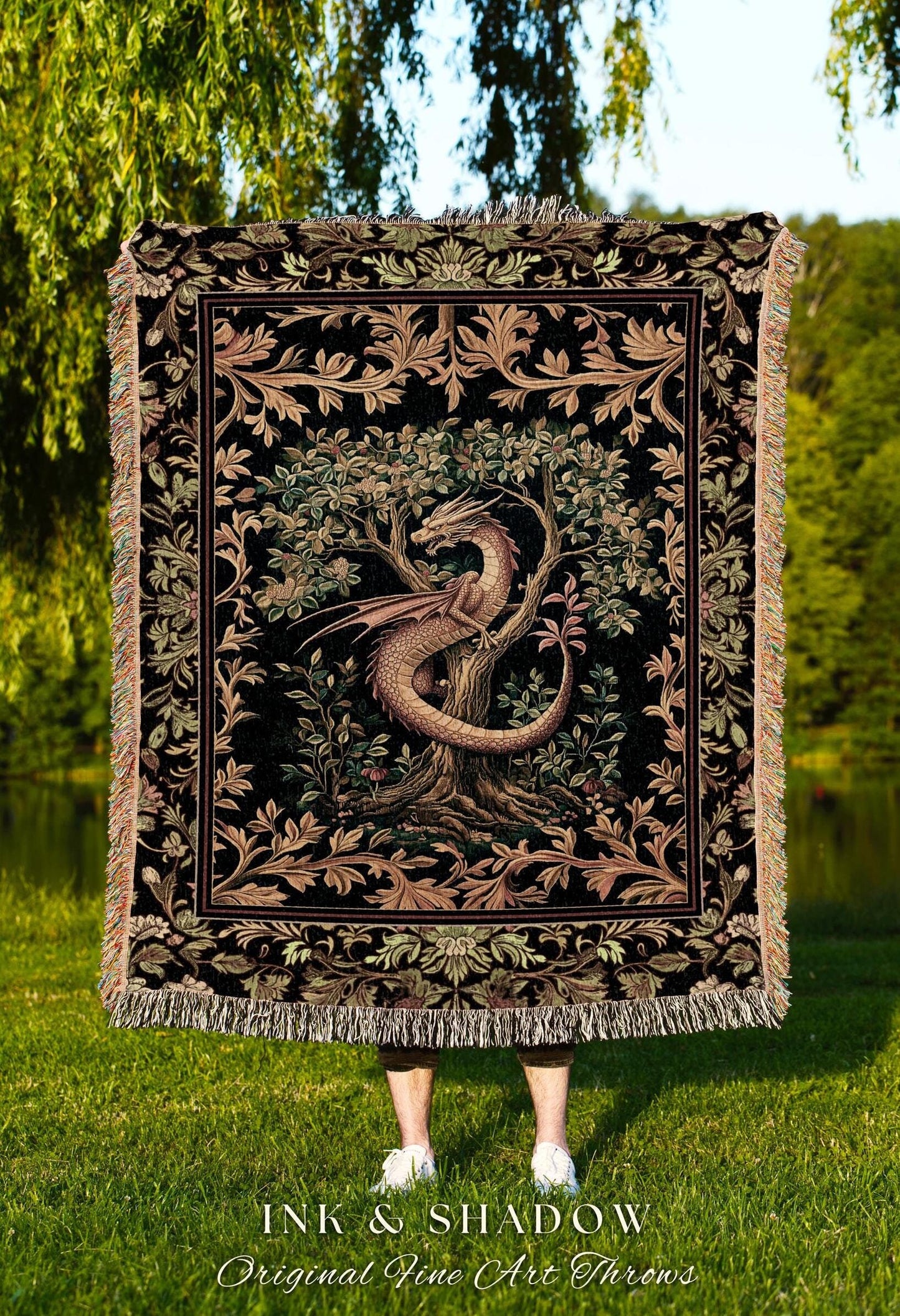 May include: A woven tapestry throw blanket features a dragon coiled around a tree in a lush garden. The design is in shades of dark brown, beige, and green on a black background.  The throw is bordered with an ornate floral pattern.  Text on the image reads: &#39;INK & SHADOW Original Fine Art Throws&#39;.