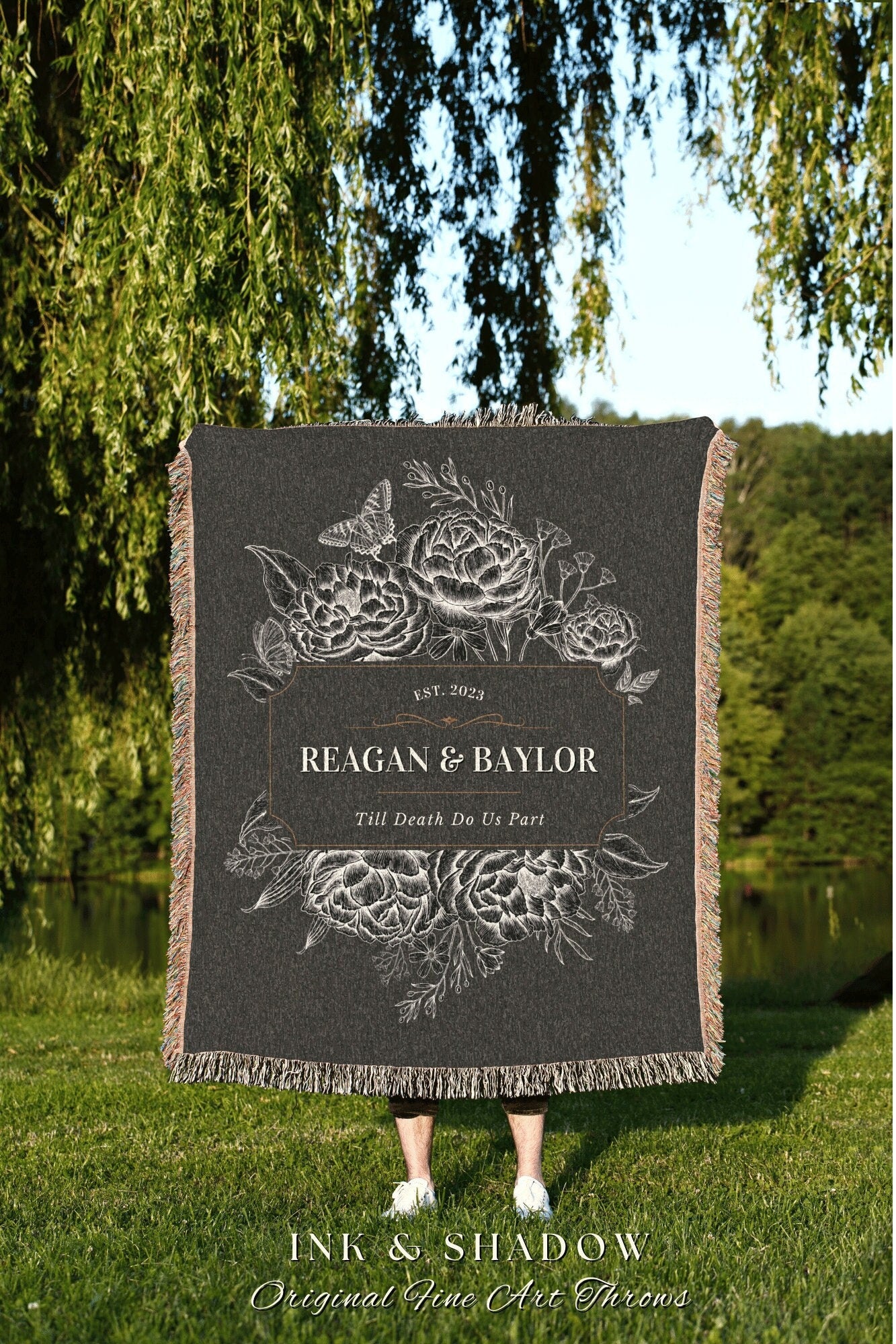 May include: A black woven throw blanket with a white floral design and the text &#39;EST. 2023 REAGAN & BAYLOR Till Death Do Us Part&#39; in a gold frame. The blanket is displayed in front of a person standing on green grass.