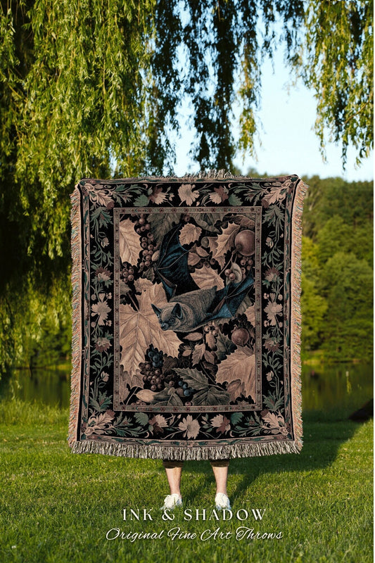 May include: A woven tapestry throw blanket with a black background and a detailed design of a bat flying through a vine of grapes. The throw blanket has a fringe border and the text &#39;INK & SHADOW Original Fine Art Throws&#39; is displayed below the blanket.