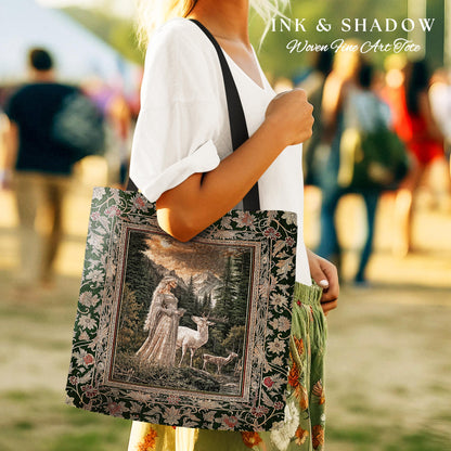 May include: A woven tote bag with a black strap. The bag features a green and black floral design with a framed image of a woman in a white dress holding a white deer in a forest setting. The text &#39;INK & SHADOW Woven Fine Art Tote&#39; is printed on the bag.