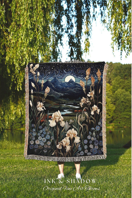 May include: A woven tapestry throw blanket with a dark blue background featuring a mountain range, a full moon, a river, and white flowers. The text &#39;INK & SHADOW Original Fine Art Throws&#39; is at the bottom of the blanket.