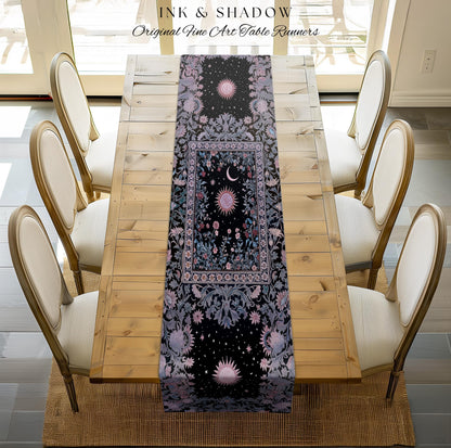 May include: A black table runner with a celestial design featuring suns, moons, and stars. The runner has a floral border in shades of purple and blue. The words 'INK & SHADOW Original Fine Art Table Runners' are at the top. The runner is placed on a wooden table with six chairs.
